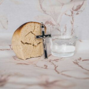 Crucifix pendant on bread beside glass