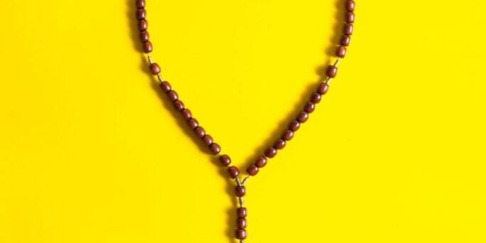 A heart-shaped rosary with a wooden cross placed on a vibrant yellow background.