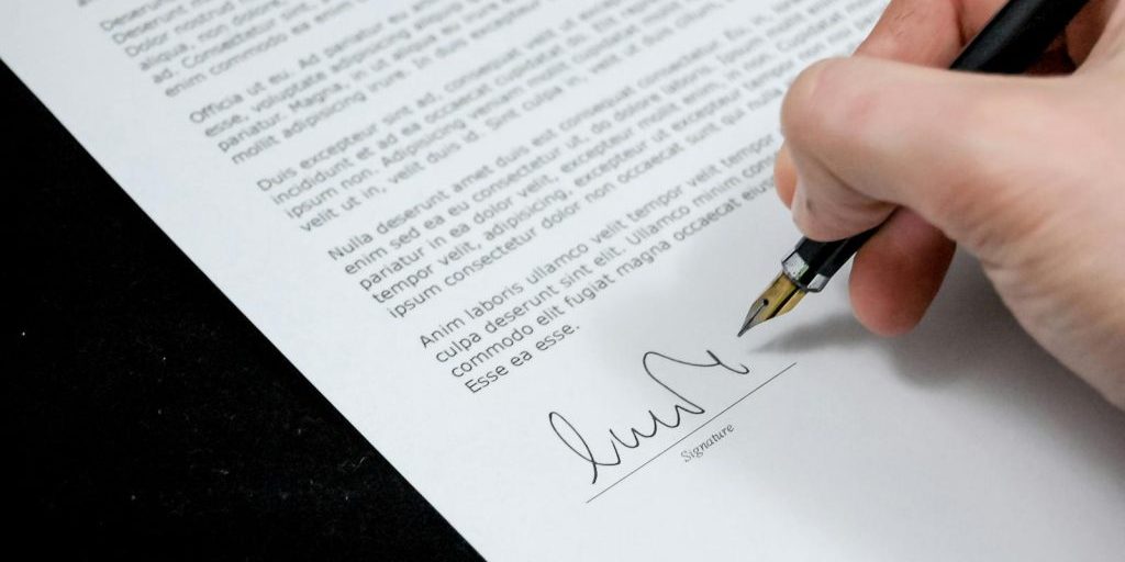 Close-up of a hand signing a formal document with a fountain pen, indicating agreement.