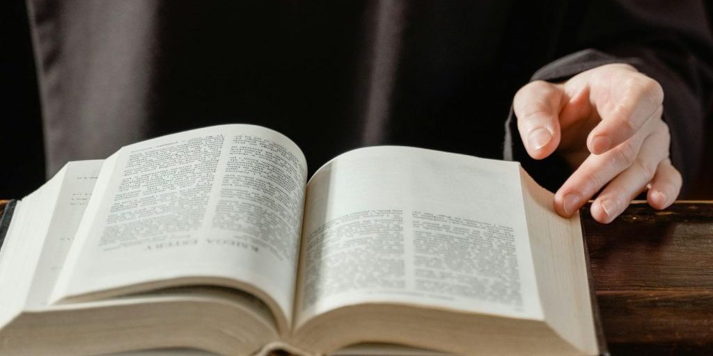 Close-up of a person turning pages of an open Bible on a wooden desk.