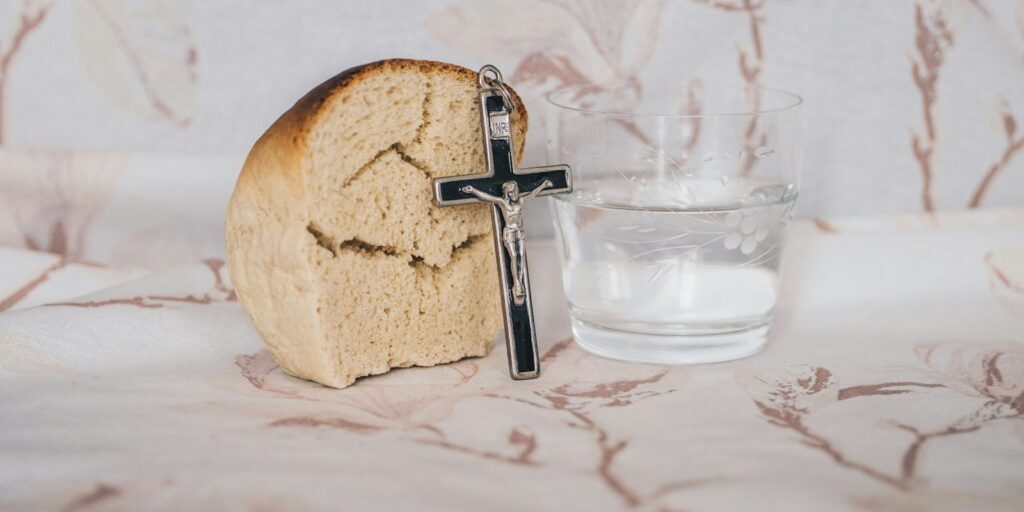 Crucifix pendant on bread beside glass